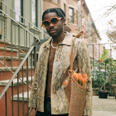 Prince Harvey standing on a Brooklyn stoop dressed in snakeskin jacket, a string of pearls and leather pants, with a bouquet of tulips in a tote bag tucked under his arm, December 2020.